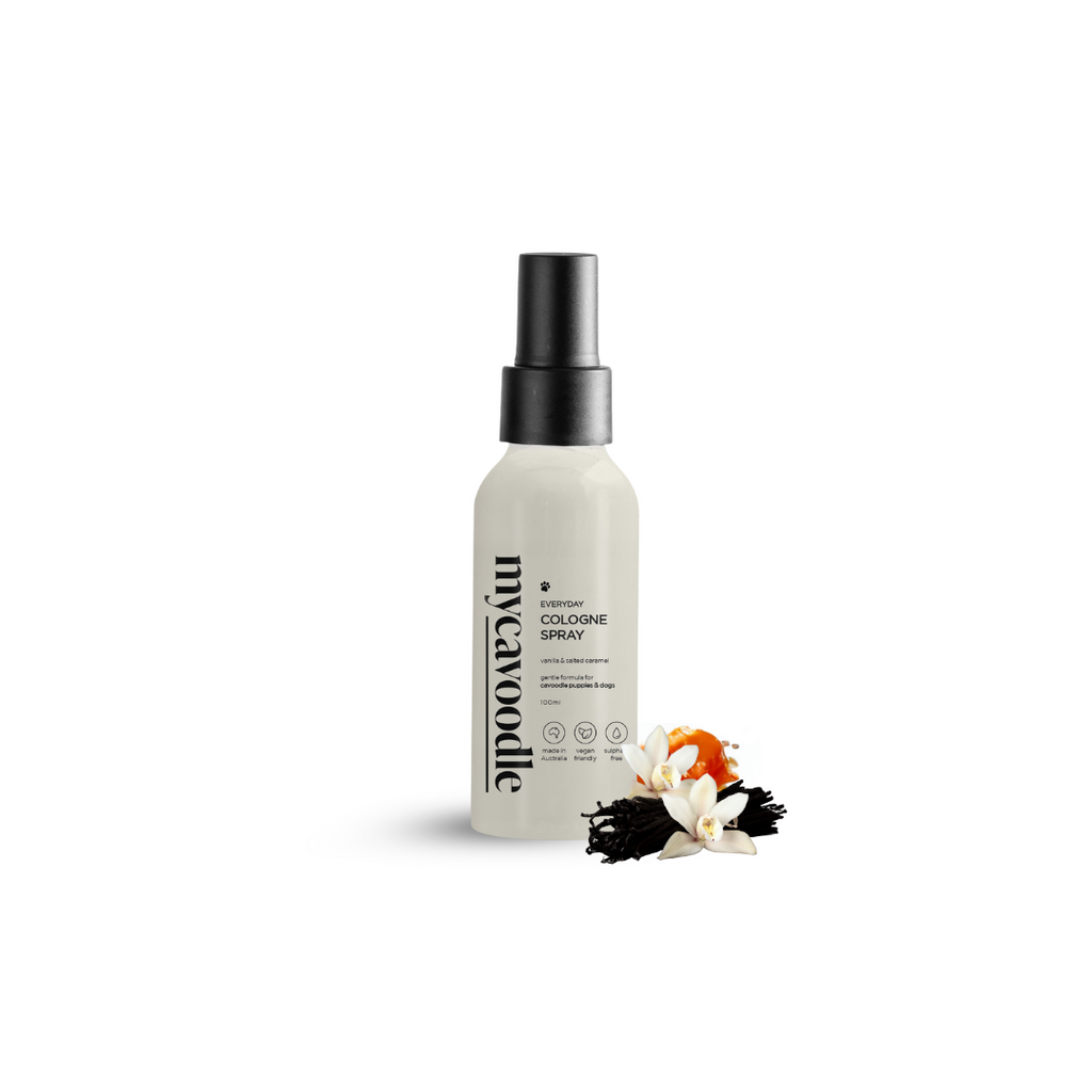 A bottle of Vanilla & Salted Caramel fragrance cologne for dogs with a spray dispenser, accompanied by a decorative flower.